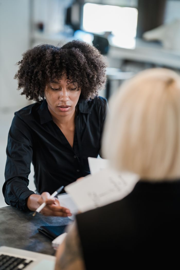 Two women collaborate on business documents in a modern office setting.